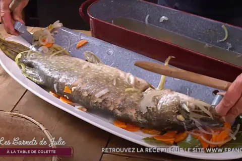 Un brochet au court-bouillon, prêt à être servi avec une mayonnaise maison. Il est garni de carottes et d'oignons.