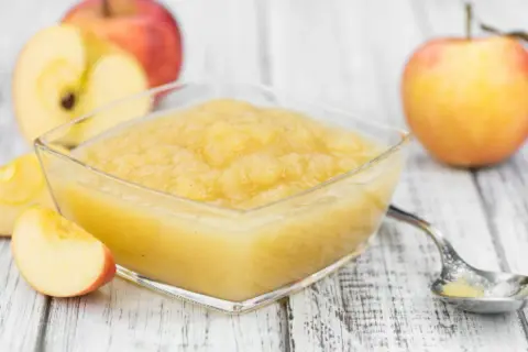 Un bol de compote pommes poires maison, avec des pommes fraîches coupées en arrière-plan.