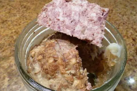 Un bocal de marmiton pâté de sanglier en bocaux stérilisés, avec une tranche de pâté posée sur le bord.