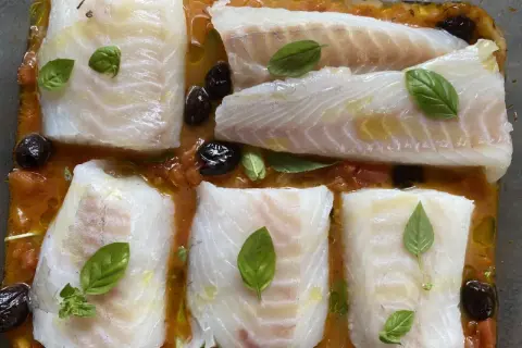 Cinq pavés de dos de cabillaud à la provençale au four, baignant dans une sauce tomate et olives, ornés de feuilles de basilic frais.