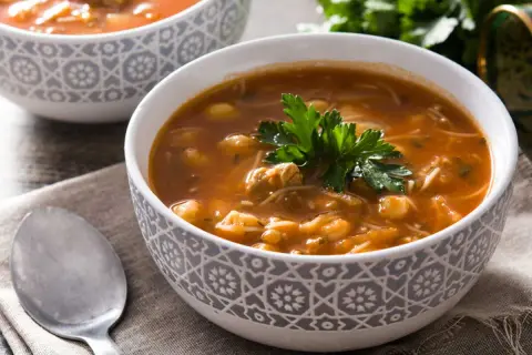 Un bol de recette harira berbère, une soupe réconfortante aux pois chiches, viande et vermicelles, garnie de persil frais.