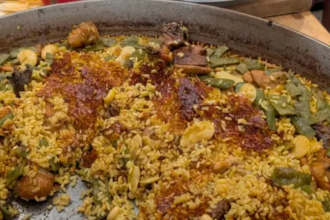 Gros plan sur une paella au feu de bois, avec du riz doré, des haricots verts, des morceaux de viande et une croûte croustillante.