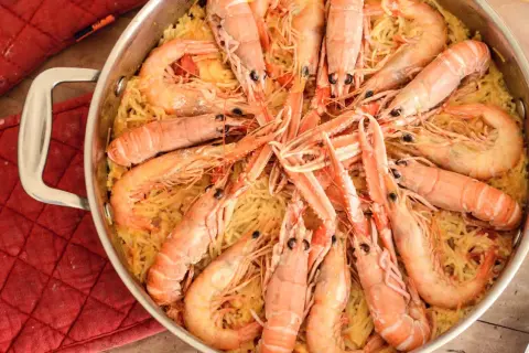 Un plat de fideuà catalana, avec des pâtes fines et des crevettes roses généreuses, prêt à être dégusté.