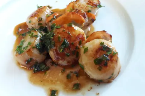 Délicieuse poêlée du pêcheur : Saint-Jacques poêlées, dorées et nappées d'une sauce savoureuse, parsemées de persil frais.