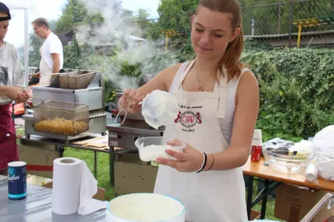 Une jeune femme prépare une recette chique de sauce crémeuse. Derrière elle, des frites dorent dans une friteuse.