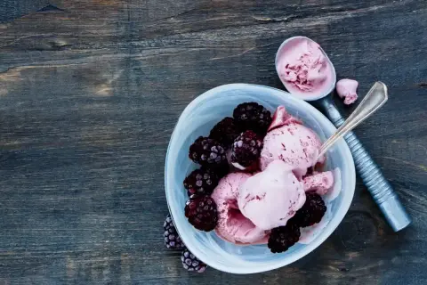 Délicieuse recette de glace avec fruits congelés et yaourt, garnie de mûres fraîches. Une cuillère sert la glace rose crémeuse.