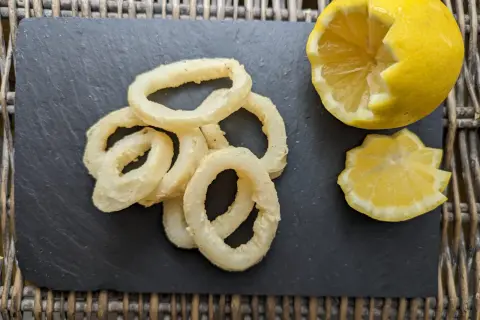 Anneaux de calamar à l'andalouse dorés et croustillants, servis avec un quartier de citron sur une ardoise.