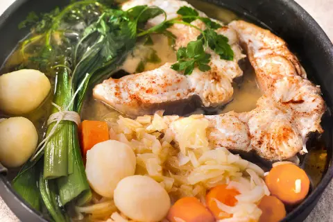Un plat appétissant de daube de congre, avec des morceaux de poisson tendres, des pommes de terre, des carottes et des poireaux, le tout mijoté dans un bouillon savoureux.