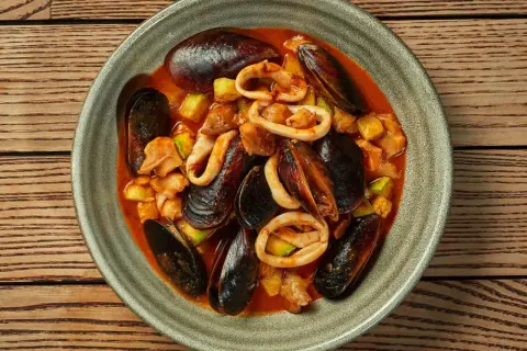 Zarzuela la vraie recette espagnole : un plat de fruits de mer savoureux avec des moules, des calamars et des légumes dans une sauce rouge.