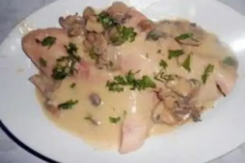 Délicieux jambon braisé au cidre, nappé d'une sauce crémeuse aux champignons et parsemé de persil frais. Un plat réconfortant.