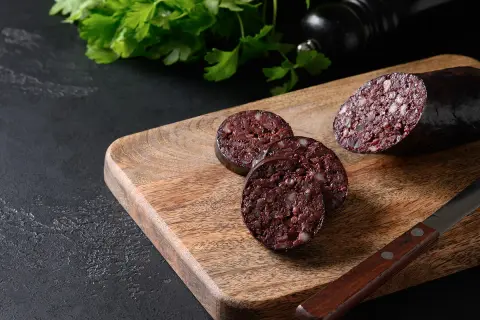 Tranché sur une planche en bois, un boudin noir froid révèle sa texture riche. Du persil frais et un moulin à poivre complètent la scène.