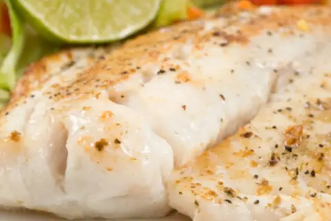 Filet de turbot au four en papillote, tendre et savoureux, servi avec une tranche de citron vert et des légumes croquants.