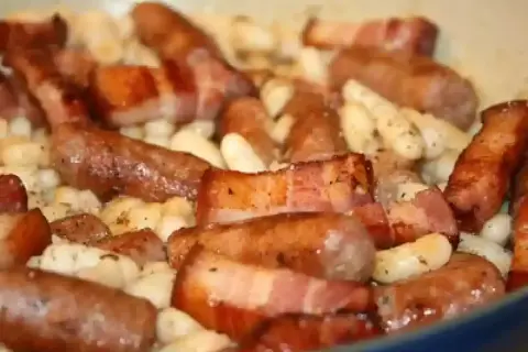 Saucisses catalanes enveloppées de lard, mijotant avec des haricots blancs. Une recette savoureuse à découvrir.