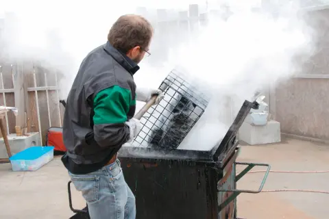 Un homme en tenue de travail manipule une grille au-dessus d'un récipient fumant, peut-être pour un gigot bitume.