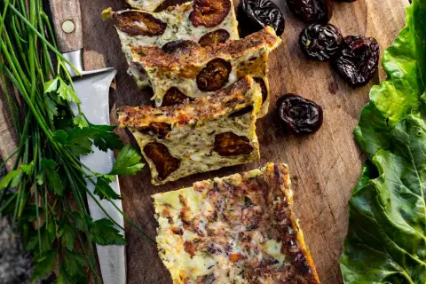 Tranches de **punti salé** aux pruneaux, sur une planche en bois, avec des herbes fraîches et des feuilles vertes.