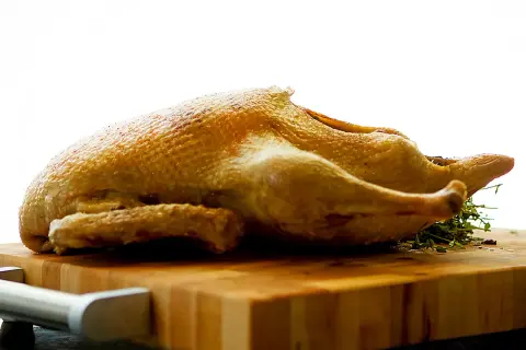 Canard entier doré, prêt pour une recette tanche entière au four. Sur une planche en bois, avec des herbes.