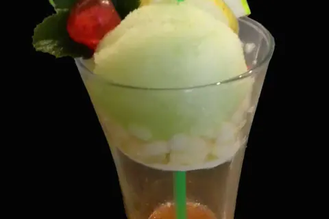 Un trou normand rafraîchissant avec une boule de glace vanille, des morceaux de fruits et une cerise.