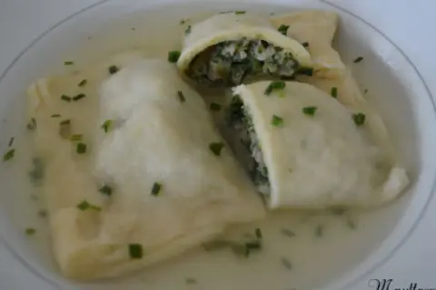 Trois maultaschen à la poêle, généreusement garnies de légumes verts et de viande, baignent dans un bouillon clair, parsemé de ciboule fraîche.