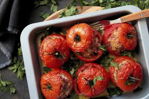 Tomates farcies à la viande dans un plat, prêtes pour le temps de cuisson. Garnies de persil frais.