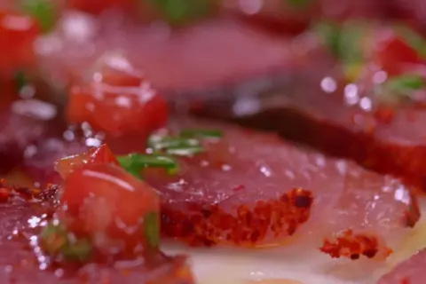Carpaccio de bonite, fines tranches de poisson cru garnies de dés de tomates rouges et d'herbes vertes, assaisonné d'épices.