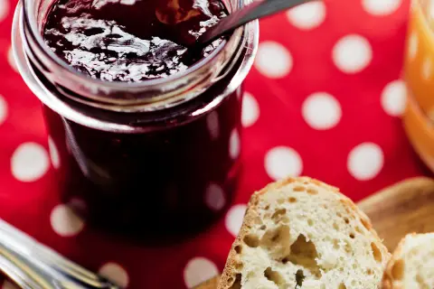 Un pot de confiture sombre, peut-être d'origine confiture de vieux garçon, sur une nappe à pois rouges. Du pain frais est prêt à être tartiné.