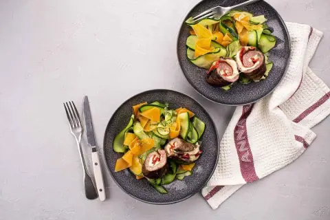 Deux assiettes de involtini de boeuf avec une salade de courgettes et carottes en rubans. Un repas léger et coloré.