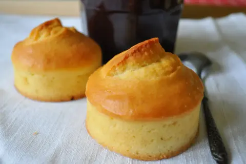 Deux petits gâteaux dorés, rappelant les vieilles recettes de gâteau à la peau de lait, sont prêts à être dégustés avec un pot de confiture sombre.