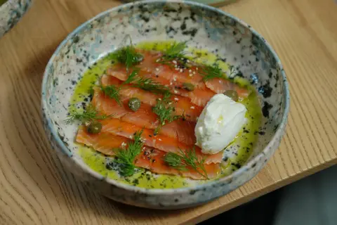Saumon gravlax maison, fines tranches de poisson cru mariné, garnies d'aneth, de câpres et d'une quenelle de crème fraîche.