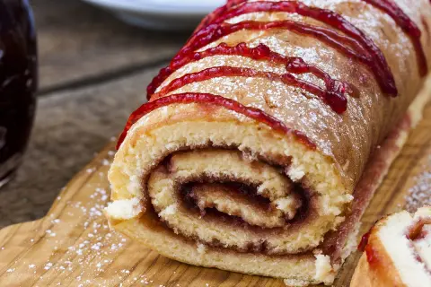Un délicieux roulé à la confiture, saupoudré de sucre glace et décoré d'un coulis rouge vif, prêt à être dégusté.