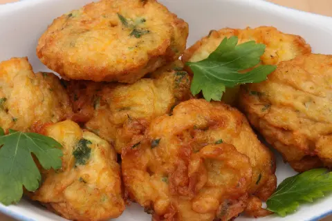 Des beignets dorés et croustillants, comme les farinettes de grand-mère, garnis d'herbes fraîches, dans un plat blanc.