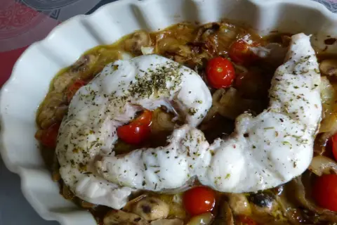 Filet de congre au four, tendre et savoureux, servi avec des tomates cerises et des champignons dans un plat blanc.