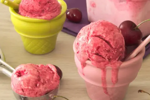 Trois coupes colorées servent une délicieuse recette sorbet cerise, avec des cerises fraîches et une cuillère à glace.