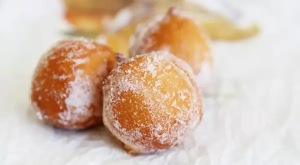 Trois beignets dorés, saupoudrés de sucre, évoquant un délicieux dessert de Côte d'Ivoire.