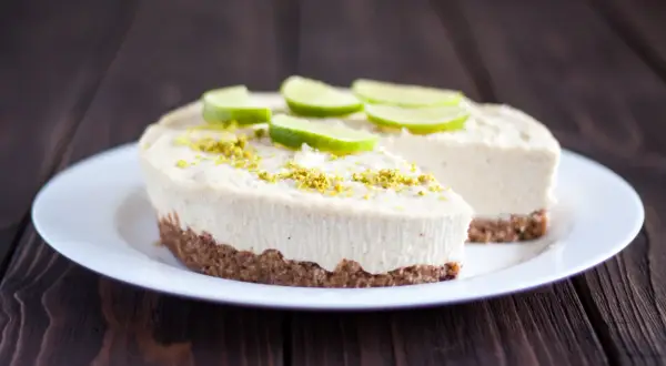 Un délicieux gâteau zéphyr crémeux, garni de fines tranches de citron vert et de zestes, sur une assiette blanche.