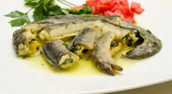 Délicieux morceaux d'anguille roulée, baignant dans une sauce dorée, parfaits pour apprendre comment préparer une anguille. Garniture de persil et tomates.