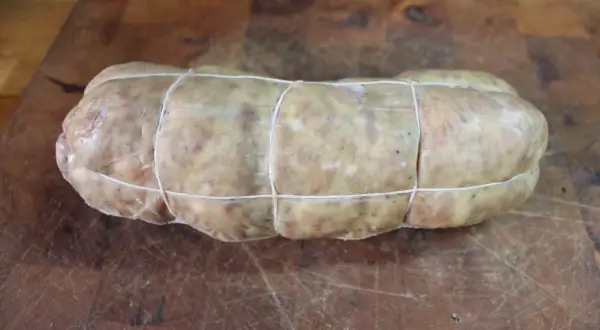 Un sabodet à la vigneronne, charcuterie artisanale ficelée, prête à être cuisinée sur une planche en bois.