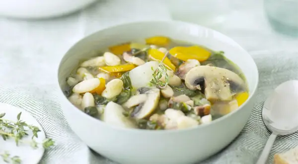 Un bol de soupe haricots blancs réconfortante avec des champignons, des carottes et des herbes fraîches.
