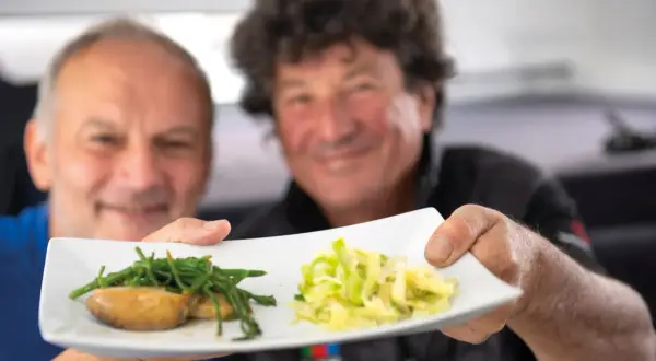 Deux hommes souriants présentent une assiette avec des ormeaux et des légumes. Une recette d'ormeau digne d'un grand chef.