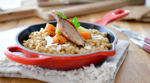 Un savoureux risotto d'épeautre garni de carottes rôties et d'une échalote confite, servi dans une cocotte rouge.