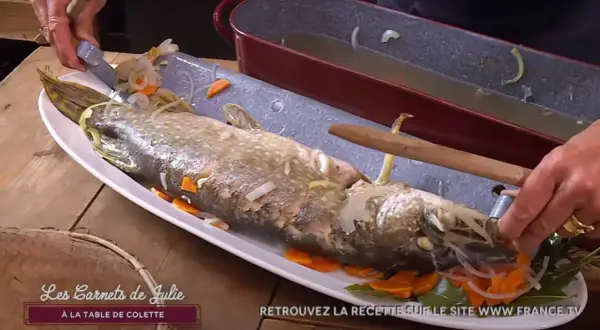 Un brochet au court-bouillon, prêt à être servi avec une mayonnaise maison. Il est garni de carottes et d'oignons.