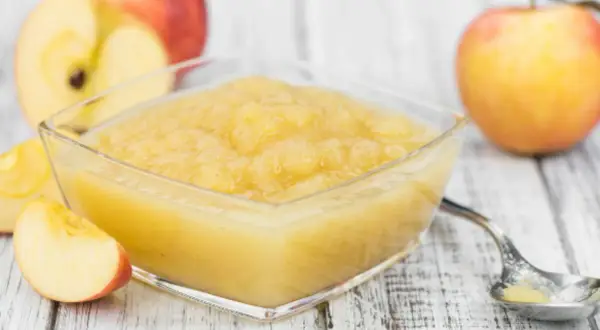 Un bol de compote pommes poires maison, avec des pommes fraîches coupées en arrière-plan.