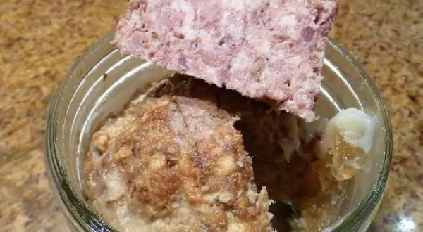 Un bocal de marmiton pâté de sanglier en bocaux stérilisés, avec une tranche de pâté posée sur le bord.