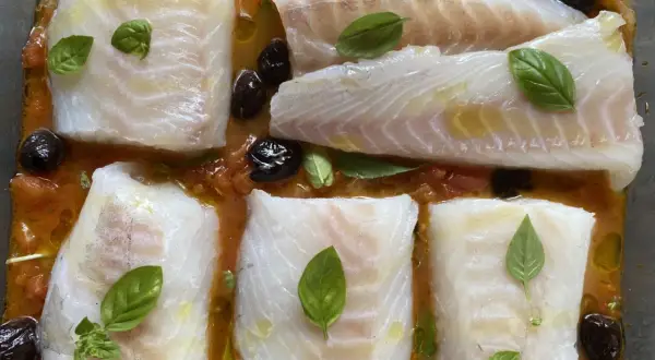 Cinq pavés de dos de cabillaud à la provençale au four, baignant dans une sauce tomate et olives, ornés de feuilles de basilic frais.