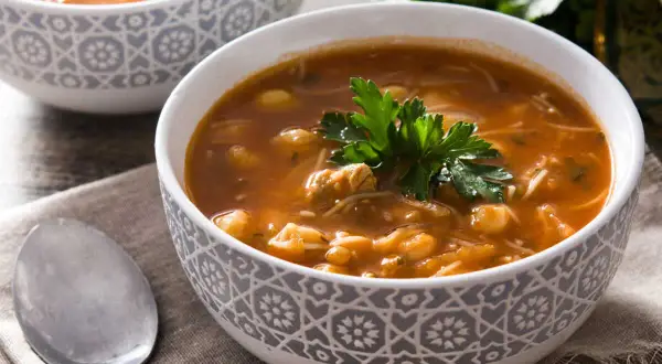 Un bol de recette harira berbère, une soupe réconfortante aux pois chiches, viande et vermicelles, garnie de persil frais.