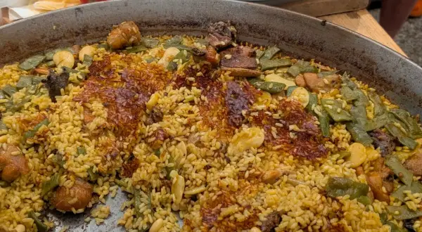 Gros plan sur une paella au feu de bois, avec du riz doré, des haricots verts, des morceaux de viande et une croûte croustillante.