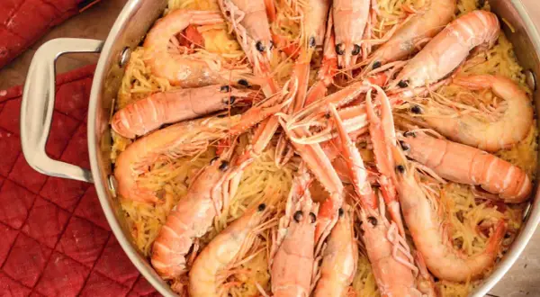 Un plat de fideuà catalana, avec des pâtes fines et des crevettes roses généreuses, prêt à être dégusté.