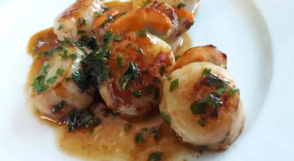 Délicieuse poêlée du pêcheur : Saint-Jacques poêlées, dorées et nappées d'une sauce savoureuse, parsemées de persil frais.