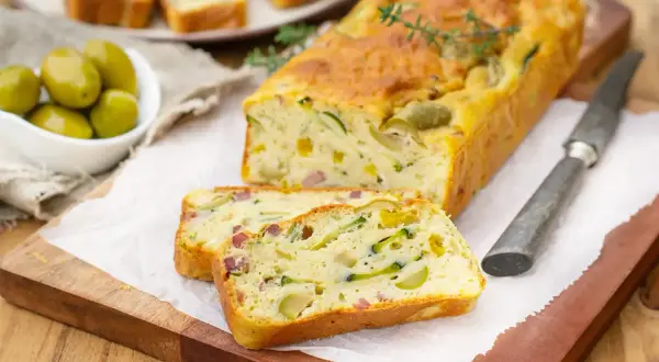 Savoureux cake salé aux courgettes et olives, parfait pour une recette d'oreille d'ours. Servi tranché sur une planche en bois.