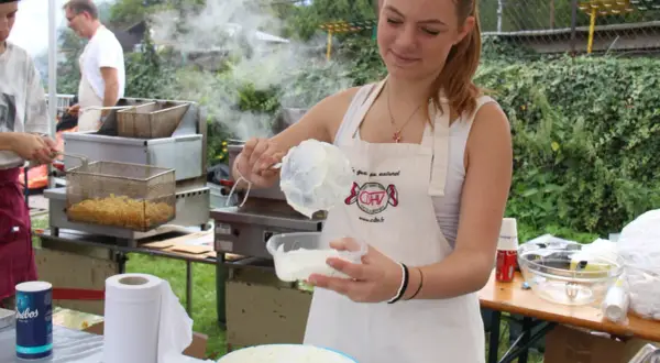 Une jeune femme prépare une recette chique de sauce crémeuse. Derrière elle, des frites dorent dans une friteuse.