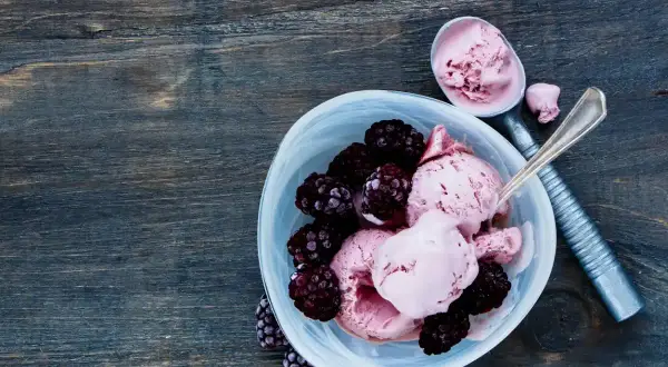 Délicieuse recette de glace avec fruits congelés et yaourt, garnie de mûres fraîches. Une cuillère sert la glace rose crémeuse.